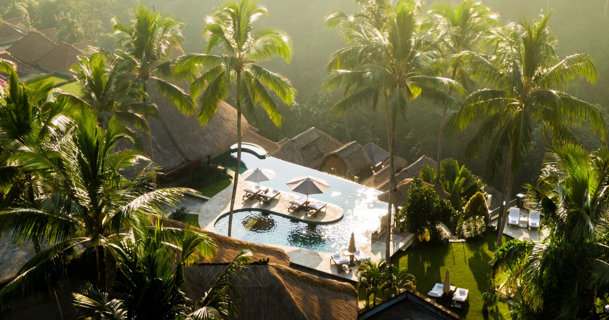 Sunlit aerial view of Viceroy Bali’s infinity pools overlooking a lush palm-filled valley, radiating tropical luxury and serenity.