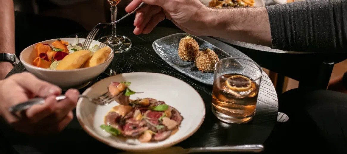 A lively, intimate dining scene at Hotel Pulitzer, with guests enjoying inventive cocktails and gourmet shared plates