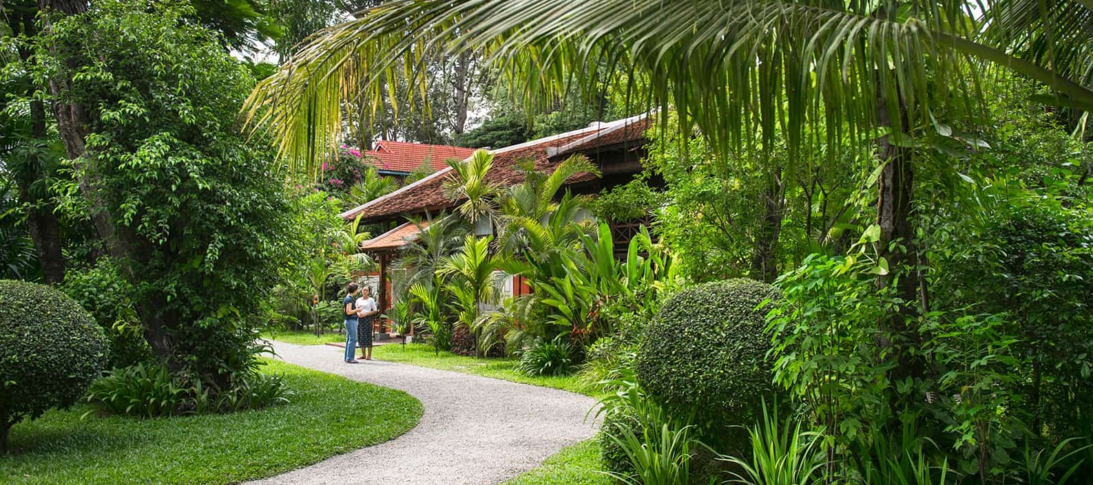 Tropical garden path leading to a traditional Khmer villa at Maison Polanka, surrounded by vibrant greenery and palm trees in Siem Reap, Cambodia