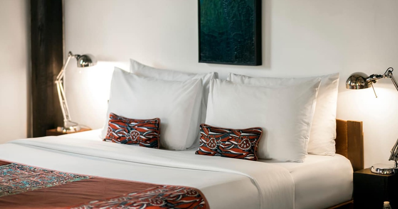 Stylish bedroom with crisp white linens, vibrant geometric patterned textiles, chrome task lamps, and contemporary teal artwork