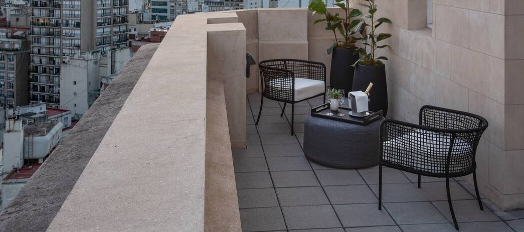 Rooftop terrace with city views, modern black chairs, potted plants, and a table set for drinks at sunset