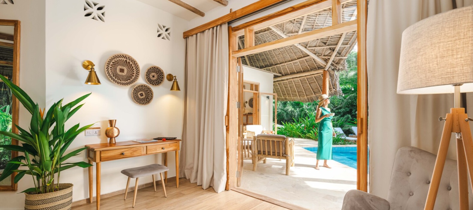 Zanzi Resort villa interior featuring natural wood furnishings, woven wall art, and open doors leading to private pool terrace