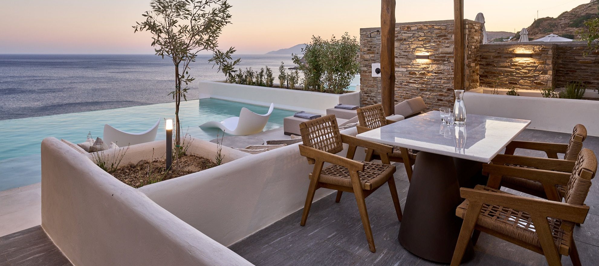Luxury terrace with infinity pool, wicker dining furniture, and panoramic Aegean Sea views at golden hour