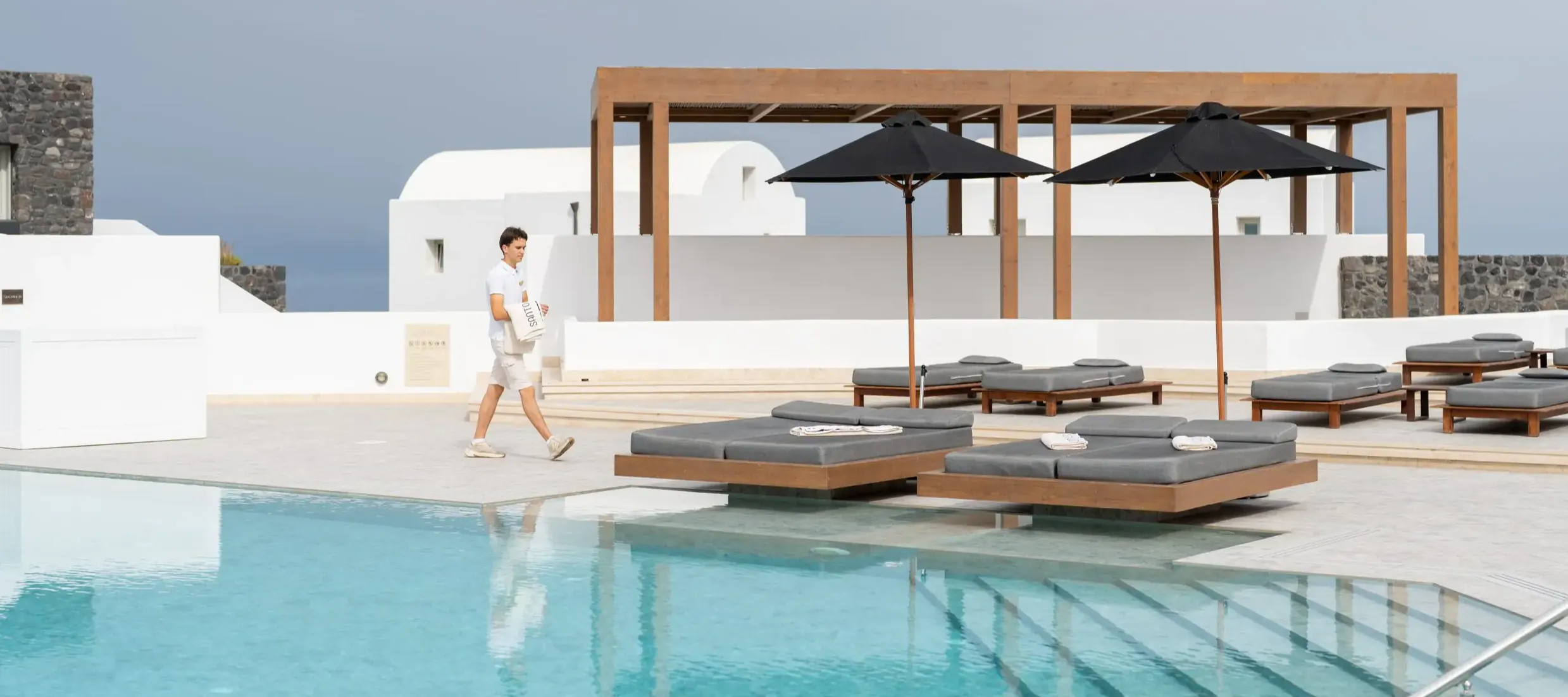 Infinity pool with modern daybeds and white Santorini architecture at Santo Pure Oia Suites