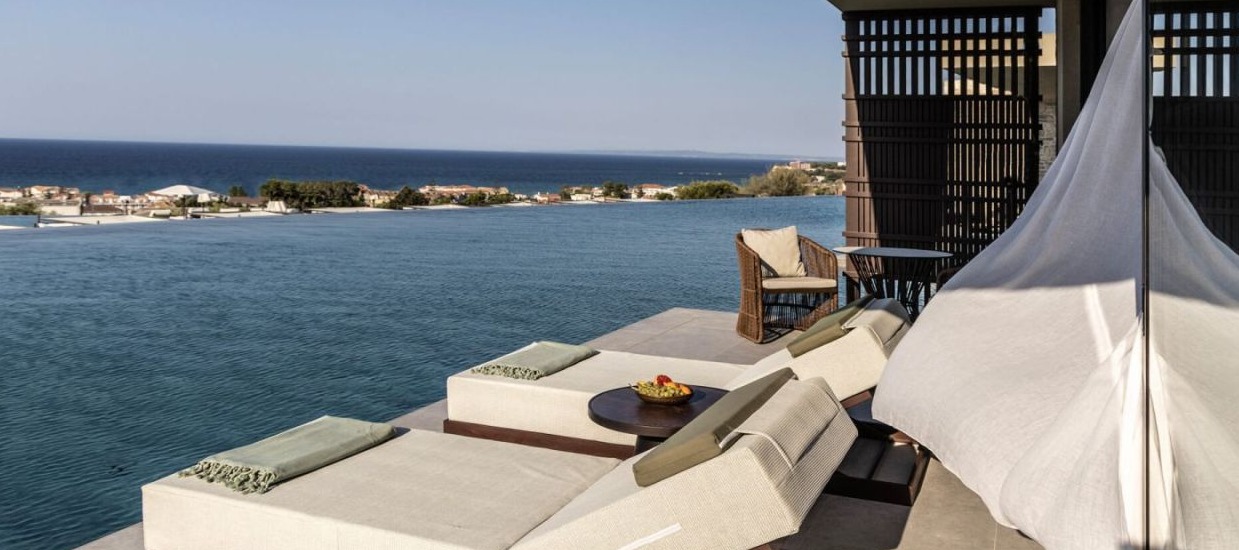 Luxury waterfront terrace with beige sun loungers, white canopy, and panoramic views
