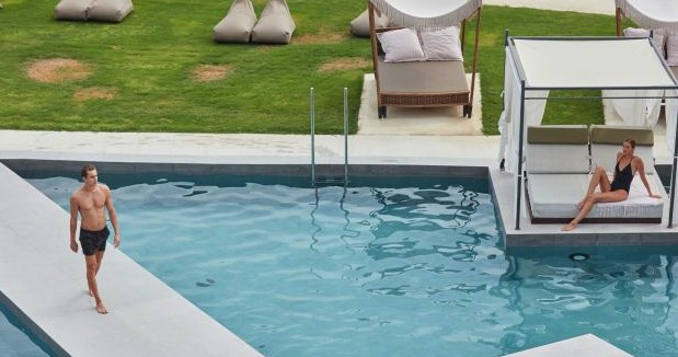 Modern resort pool with guests relaxing on white cabana beds and bean bag seating on manicured lawn