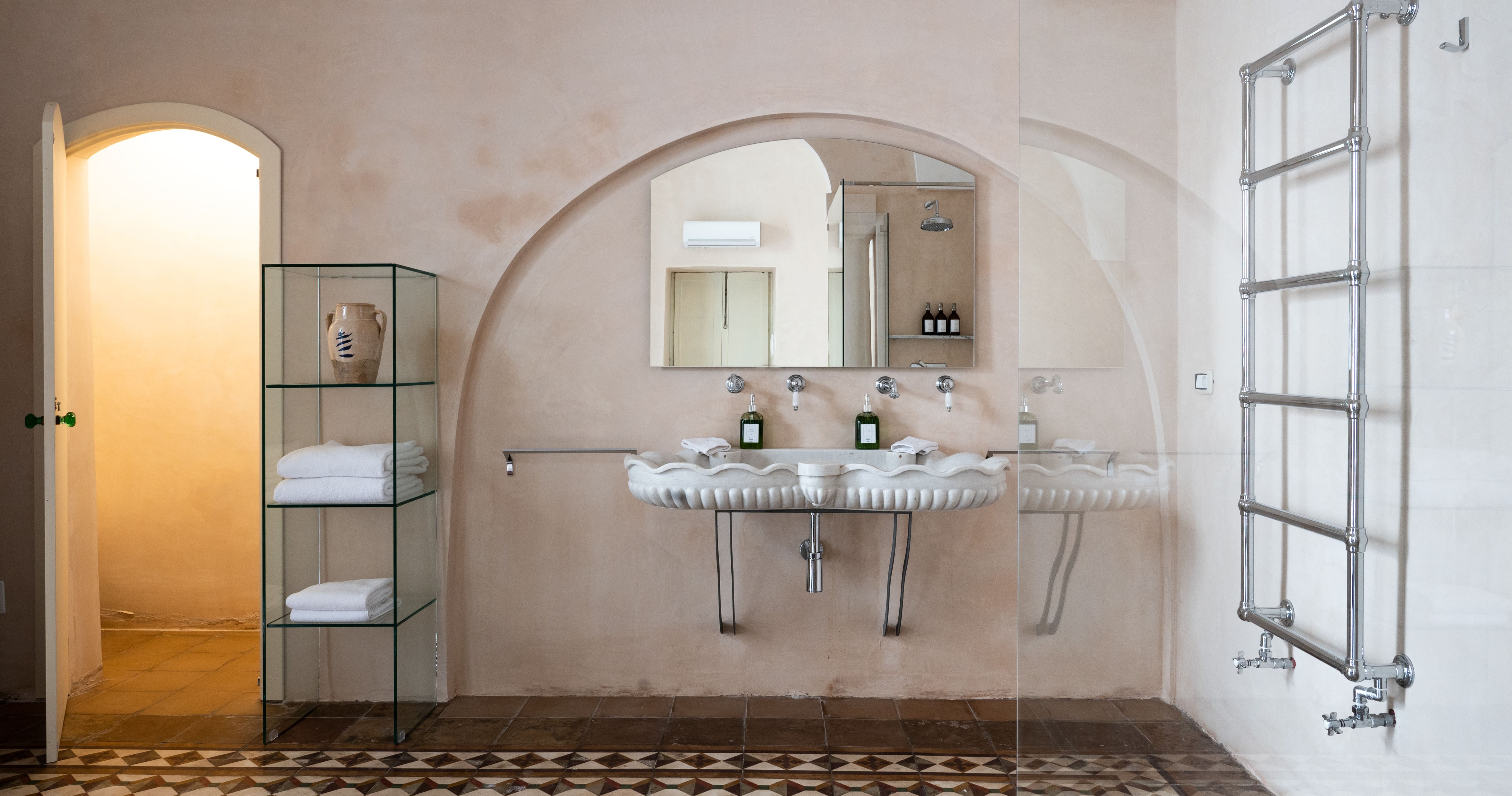 Arched bathroom with shell basin, geometric floor tiles, and glass shelving