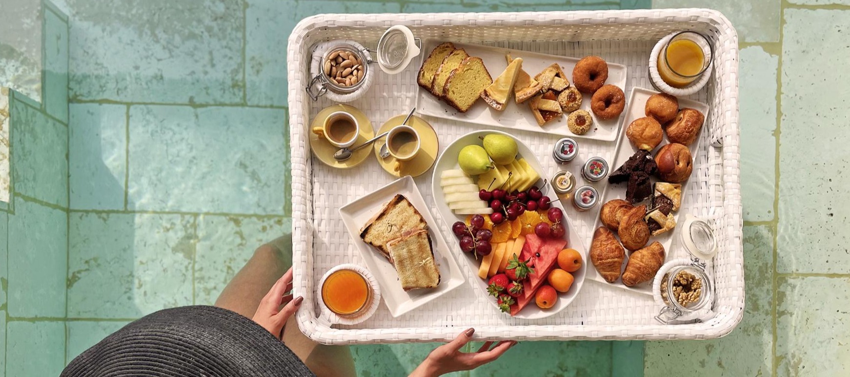 Hotel breakfast tray with pastries, fruit, coffee, and juice on turquoise tile floor