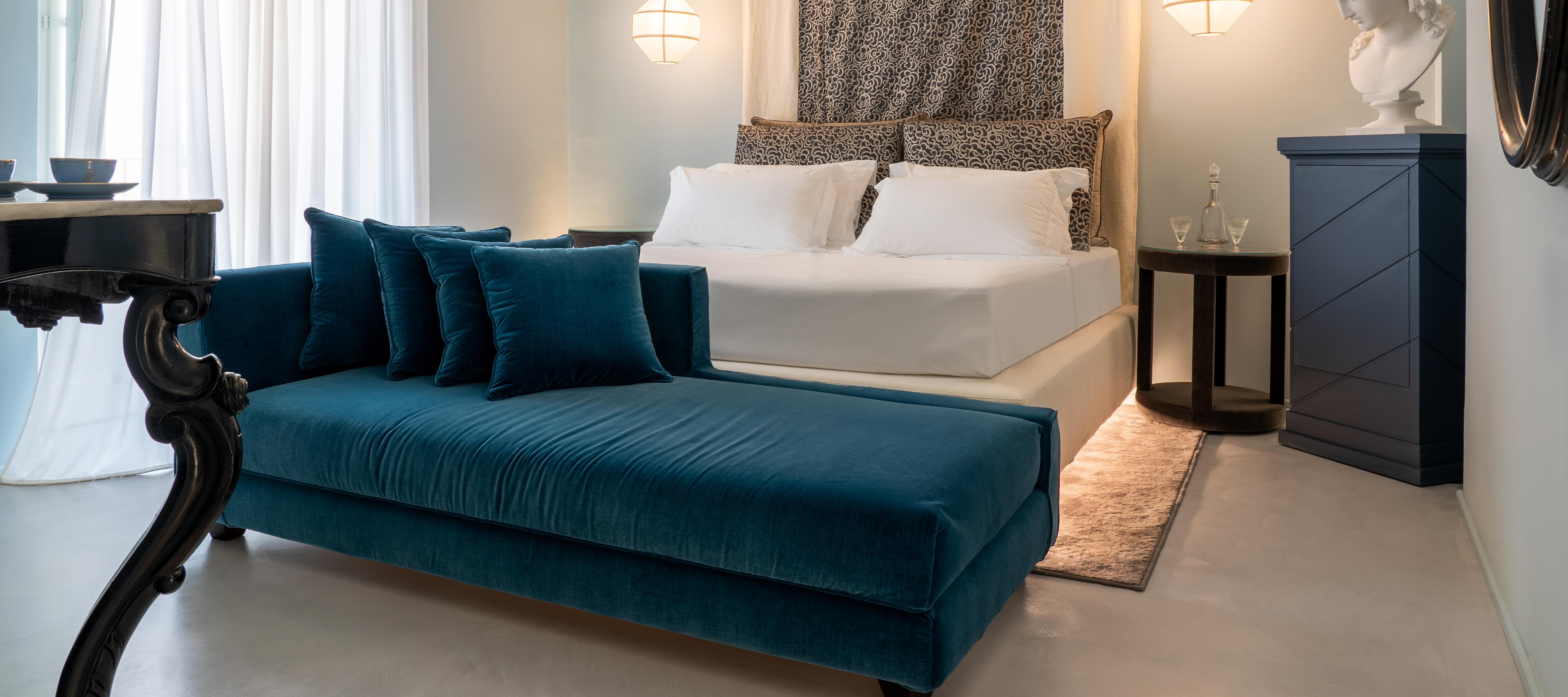 Elegant Q92 Noto superior room featuring a plush teal chaise lounge, white linen bed, and unique leopard print headboard