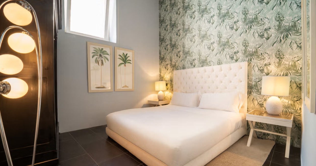 classic room featuring a tufted white headboard against a dramatic green tropical print wallpaper and dark tiled floor