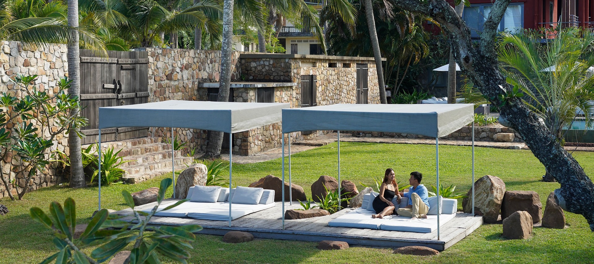 Shaded daybeds on manicured lawn with stone accents and tropical palm gardens
